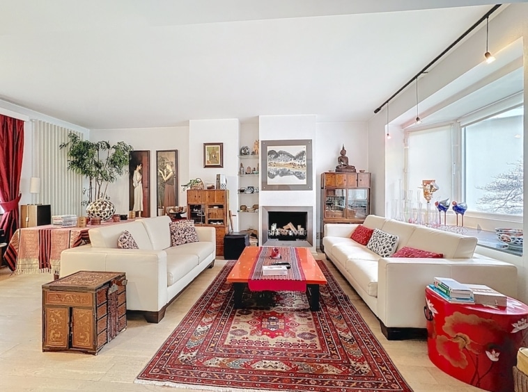 Salon lumineux avec cheminée, canapé blanc, table rouge et décoration traditionnelle élégante.
