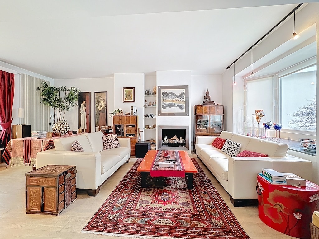 Salon lumineux avec cheminée, canapé blanc, table rouge et décoration traditionnelle élégante.