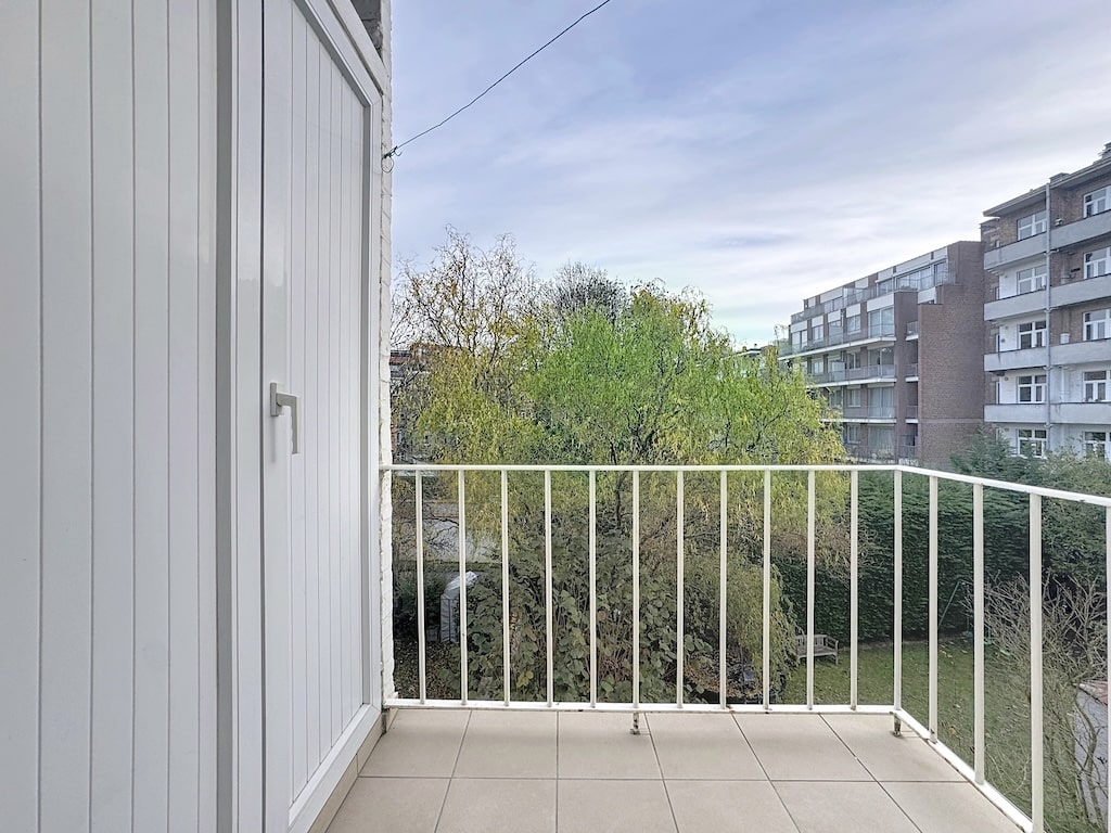 Balcon moderne avec vue sur jardin verdoyant et bâtiments urbains, ambiance calme et apaisante.