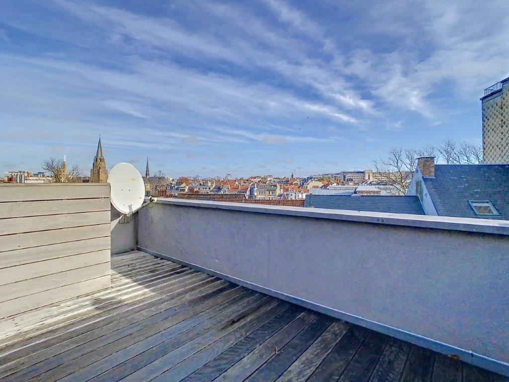 Balcon urbain en bois offrant vue sur la ville, clocher et ciel bleu.