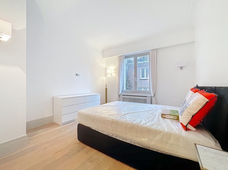 Chambre minimaliste blanche lumineuse avec lit noir, coussins rouges, mobilier épuré et sol en bois clair.