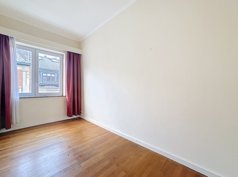 Chambre lumineuse minimaliste avec fenêtre, murs crème, sol en bois, rideaux velours bordeaux élégants.