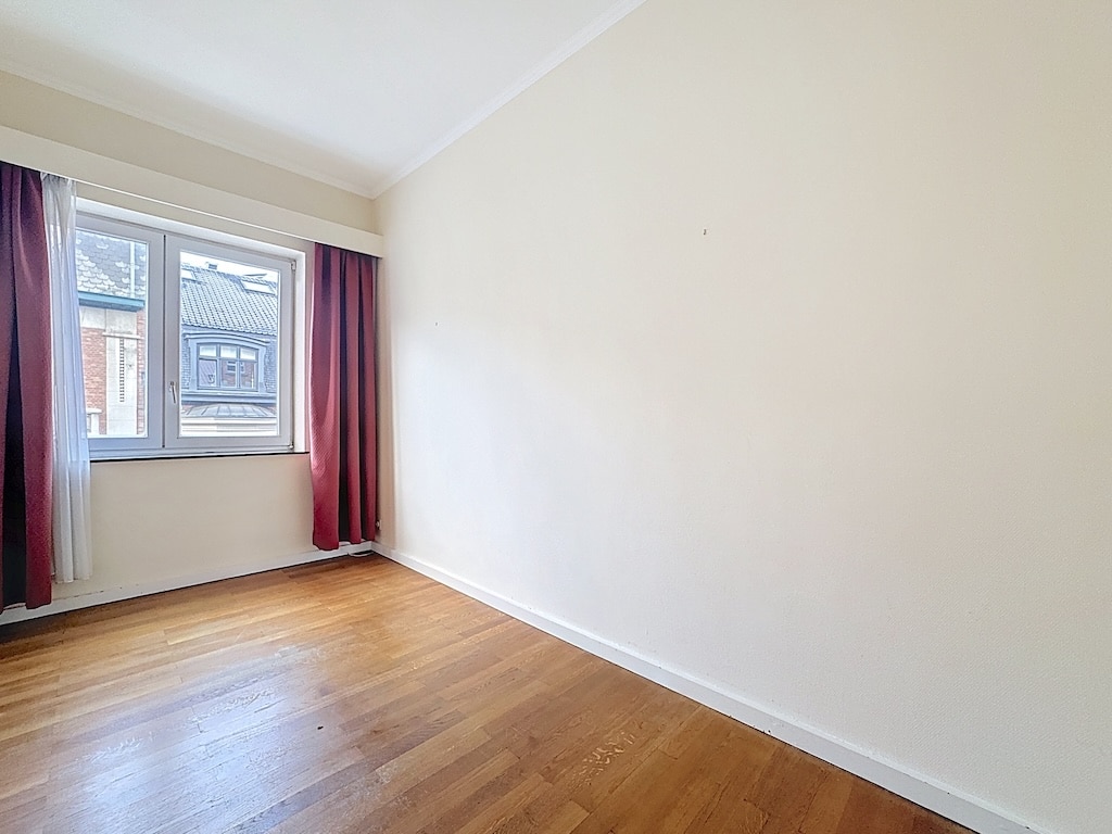 Chambre lumineuse minimaliste avec fenêtre, murs crème, sol en bois, rideaux velours bordeaux élégants.