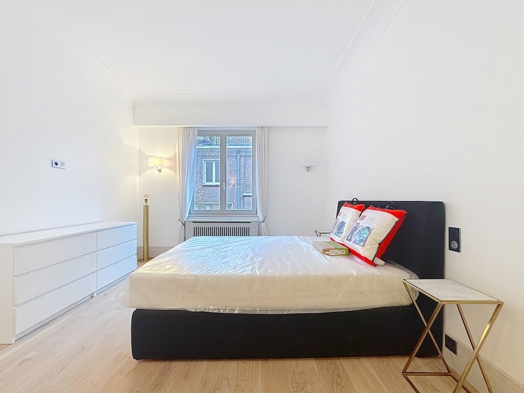 Chambre moderne lumineuse avec lit noir, mobilier minimaliste et ambiance apaisante en bois clair.