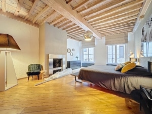 Chambre moderne et chaleureuse avec poutres en bois grand lit cheminée et fauteuil vert rétro