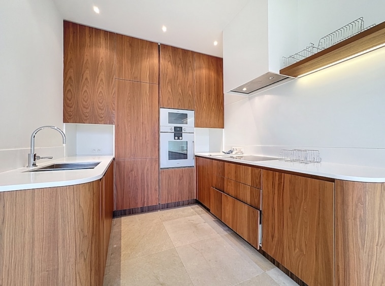 Cuisine moderne en bois foncé et blanc avec plan de travail épuré et éclairage élégant.