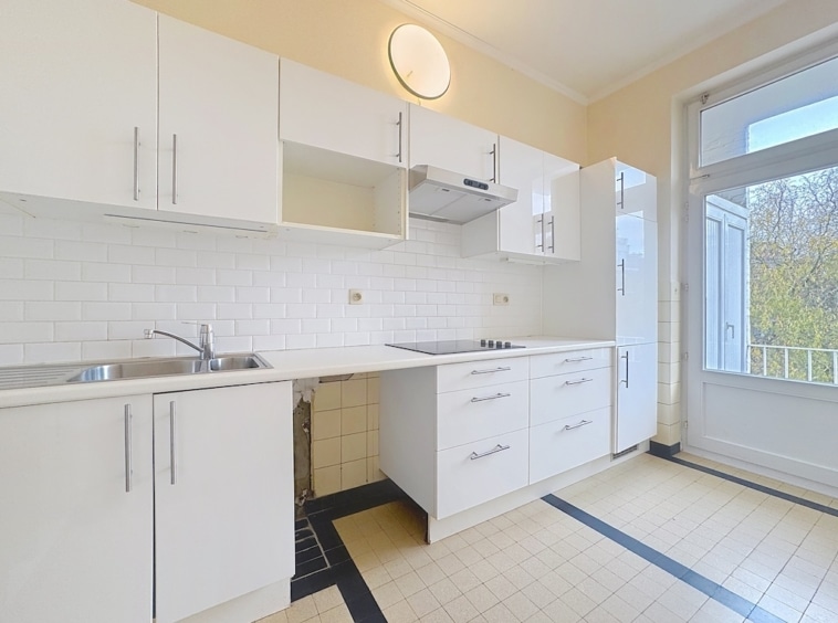 Cuisine moderne lumineuse avec meubles blancs, plan de travail clair, grande fenêtre et carrelage damier.