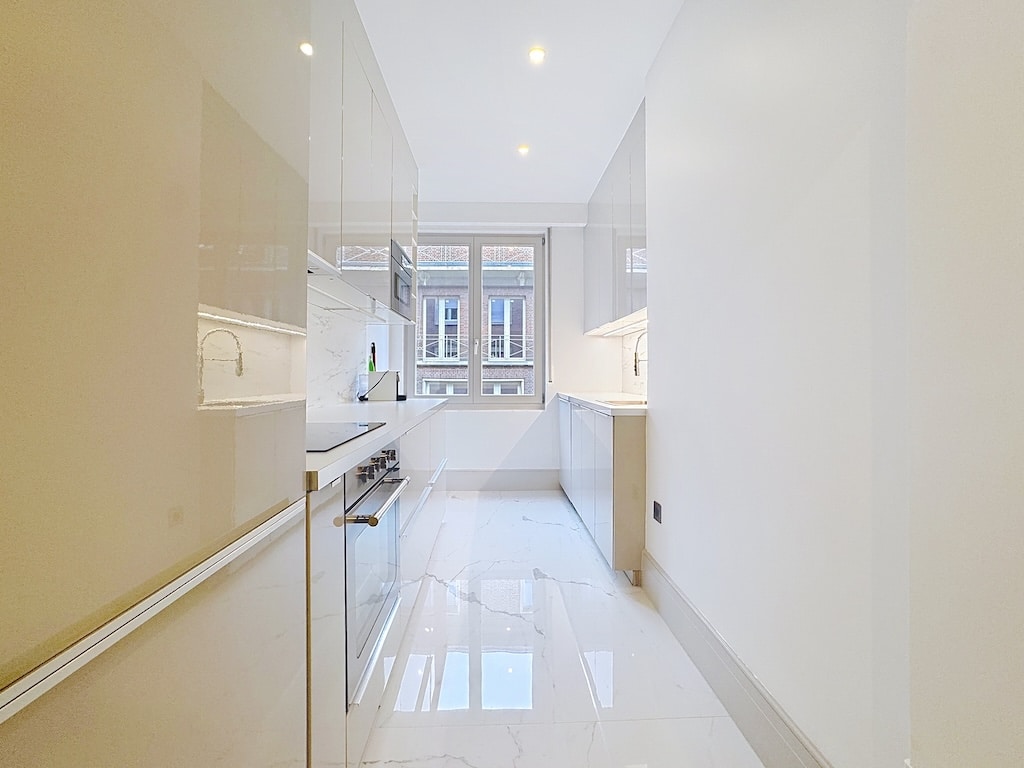 Cuisine contemporaine lumineuse avec mobilier brillant, plan blanc et grande baie vitrée.