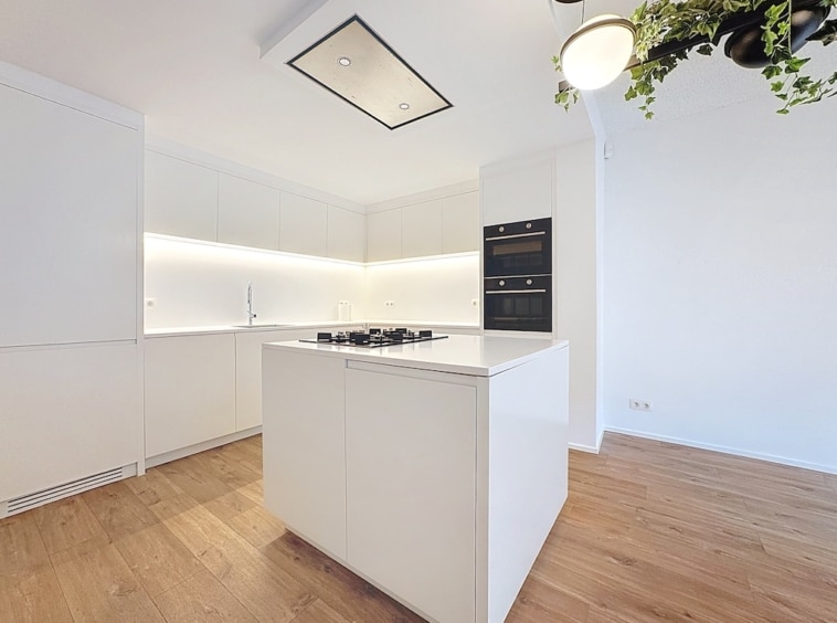 Cuisine moderne minimaliste avec îlot en bois, éclairage d’ambiance et éléments contrastés.