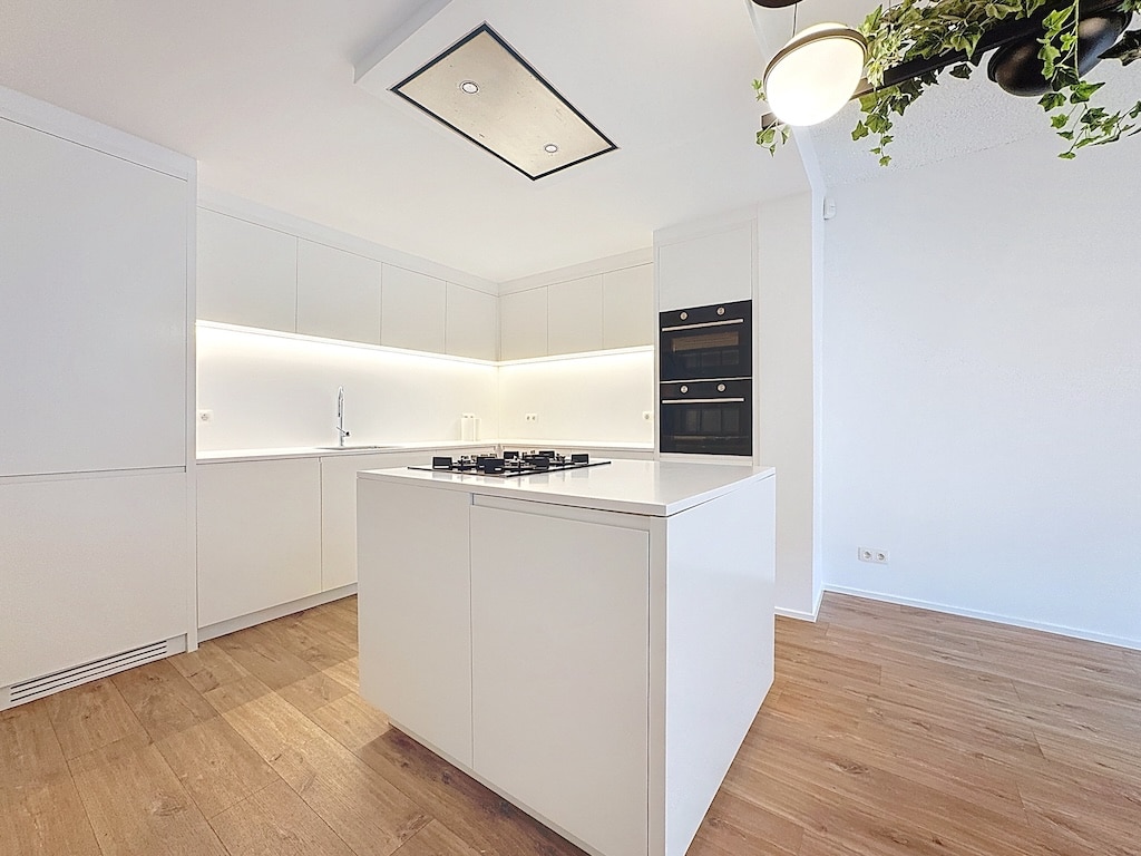 Cuisine moderne minimaliste avec îlot en bois, éclairage d’ambiance et éléments contrastés.