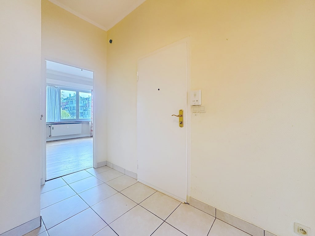 Hall lumineux avec murs jaunes, porte blanche dorée, ouverture sur pièce ensoleillée.