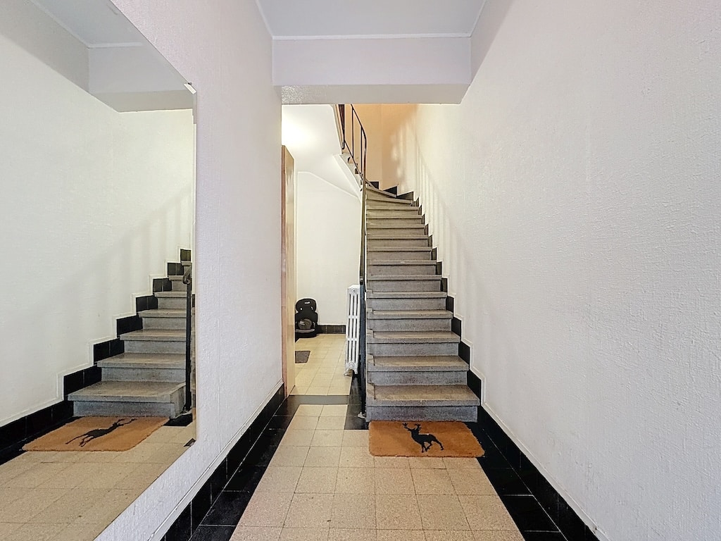Escalier intérieur blanc minimaliste avec miroirs, éclairage doux et tapis d’accueil moderne.