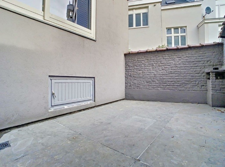 Court extérieur urbain en pavé, murs en brique grise, lumière naturelle.