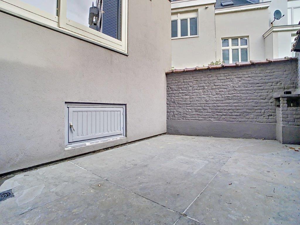 Court extérieur urbain en pavé, murs en brique grise, lumière naturelle.