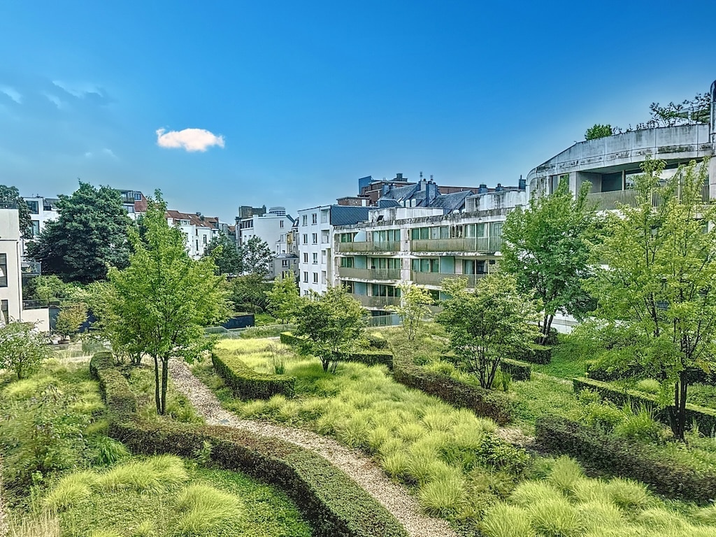 Jardin urbain moderne avec bâtiments contemporains, arbres ombrageants et ciel bleu lumineux.