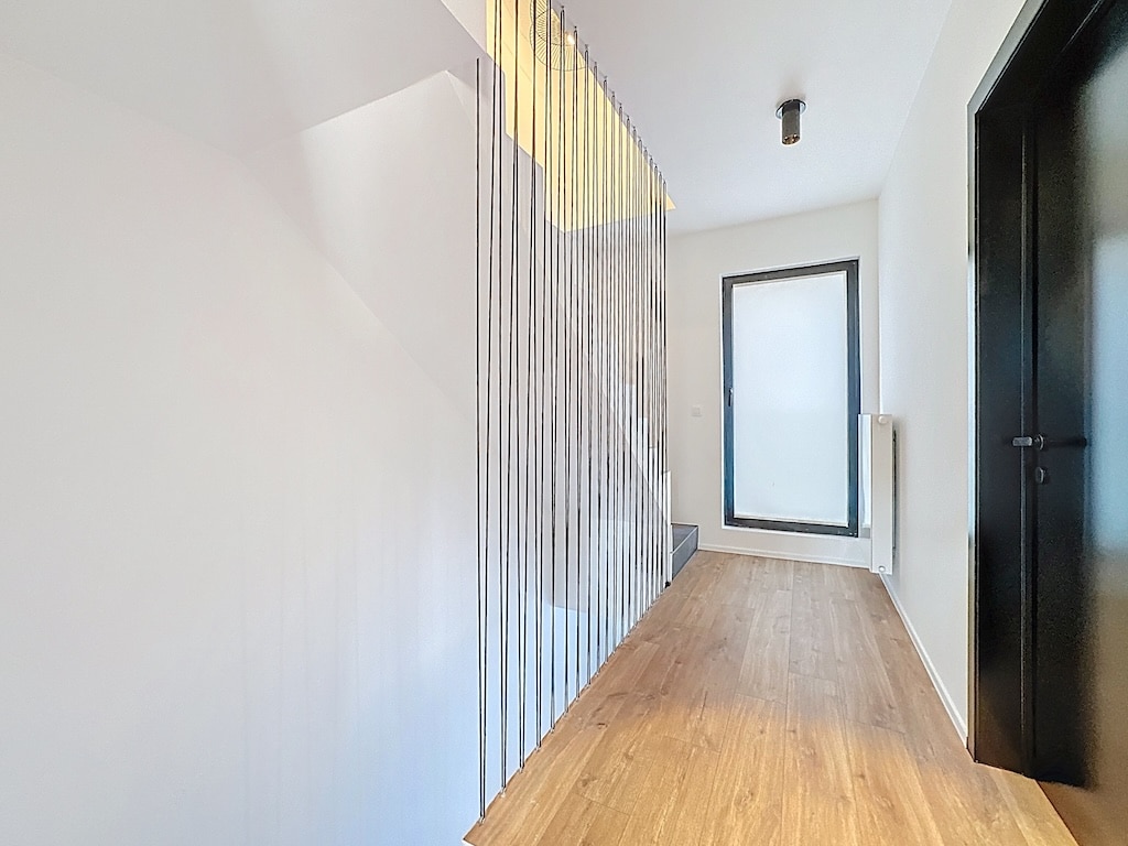 Hall dentrée moderne lumineux avec escalier en bois, murs blancs, grande fenêtre, design épuré.