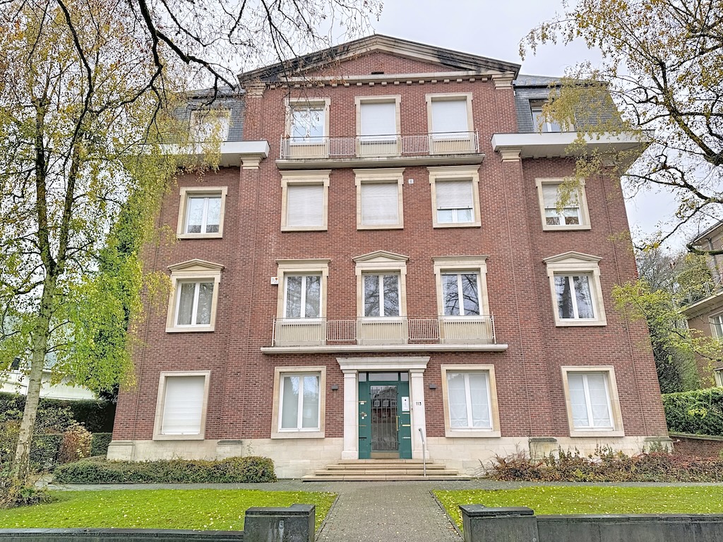 Immeuble en brique rouge avec jardin, balcons, escaliers et façade symétrique en milieu urbain.