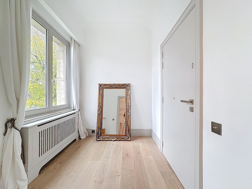 Salon minimaliste lumineux avec miroir vintage, vue verte, parquet clair et décoration élégante.