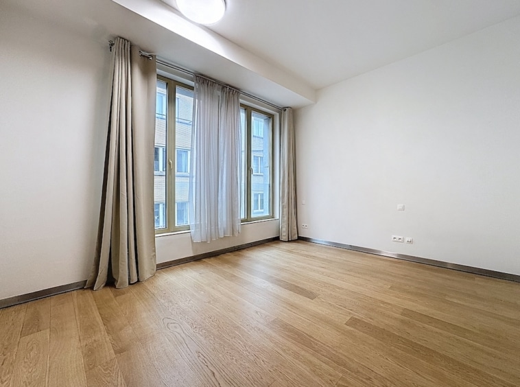 Salon lumineux avec murs blancs, sol en bois clair et grandes fenêtres modernes.