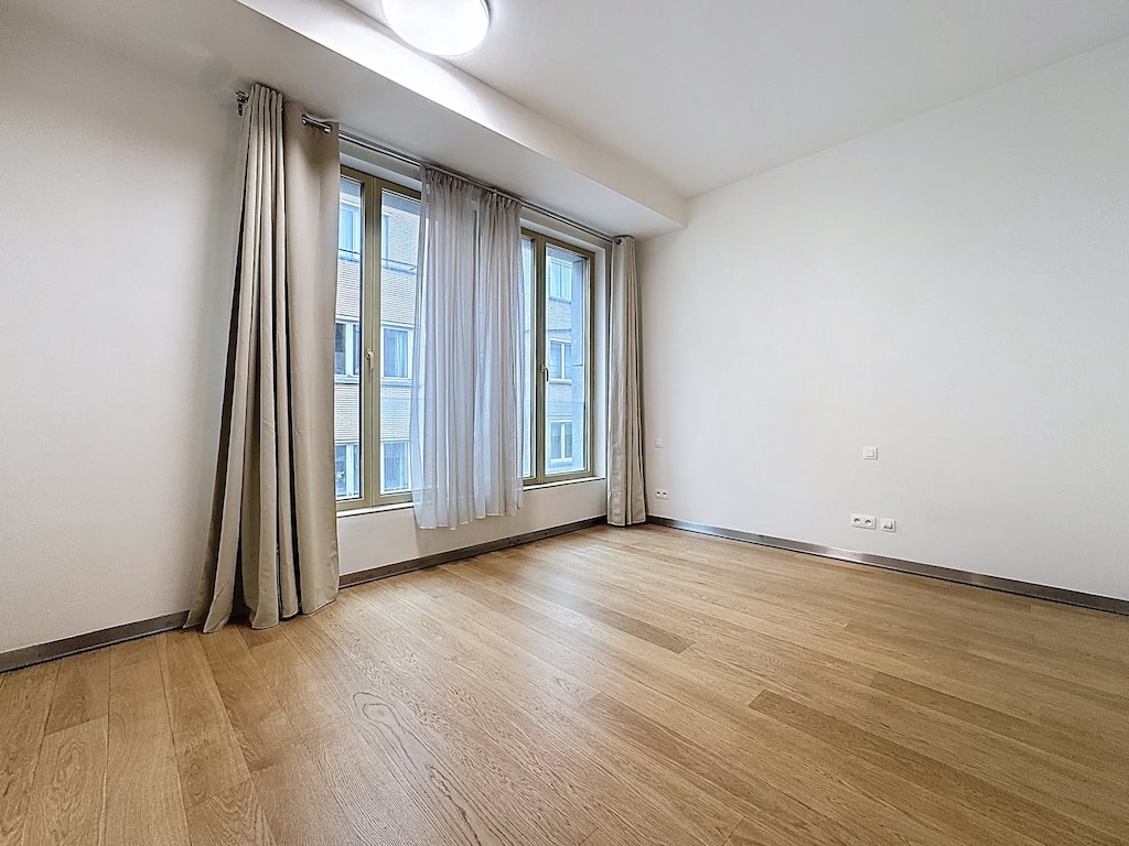 Salon lumineux avec murs blancs, sol en bois clair et grandes fenêtres modernes.