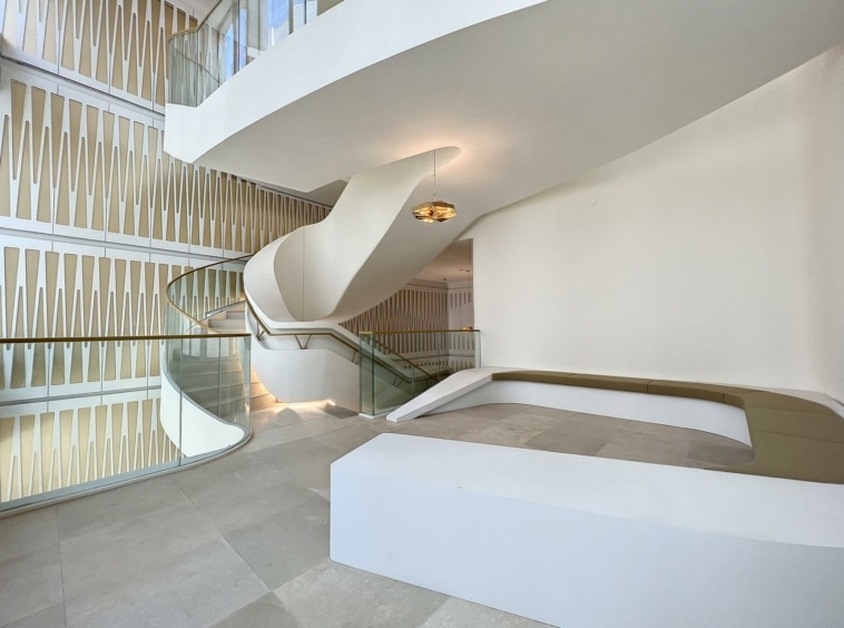 Intérieur moderne avec escalier spiral en verre, murs blancs, lumière naturelle et design minimaliste élégant.
