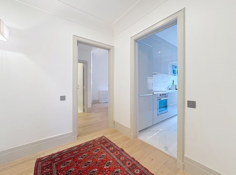 Salon moderne avec tapis rouge, cuisine minimaliste et ambiance lumineuse chaleureuse.