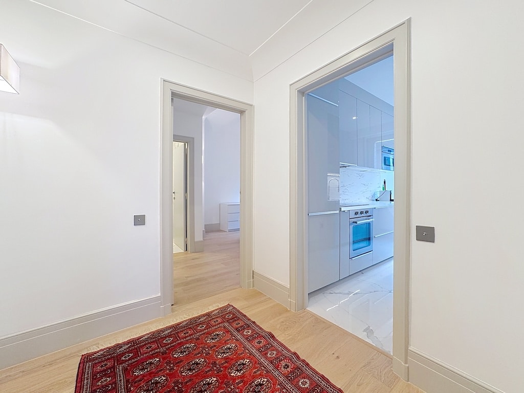 Salon moderne avec tapis rouge, cuisine minimaliste et ambiance lumineuse chaleureuse.