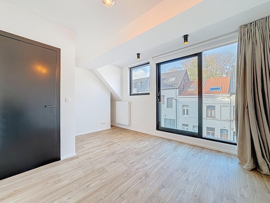 Espace moderne lumineux avec murs blancs, grande fenêtre, sol en bois clair, vue urbaine charmante.