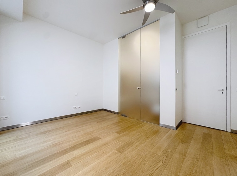 Salon minimaliste moderne avec sol en bois clair, armoire en verre dépoli et plafond avec ventilateur.