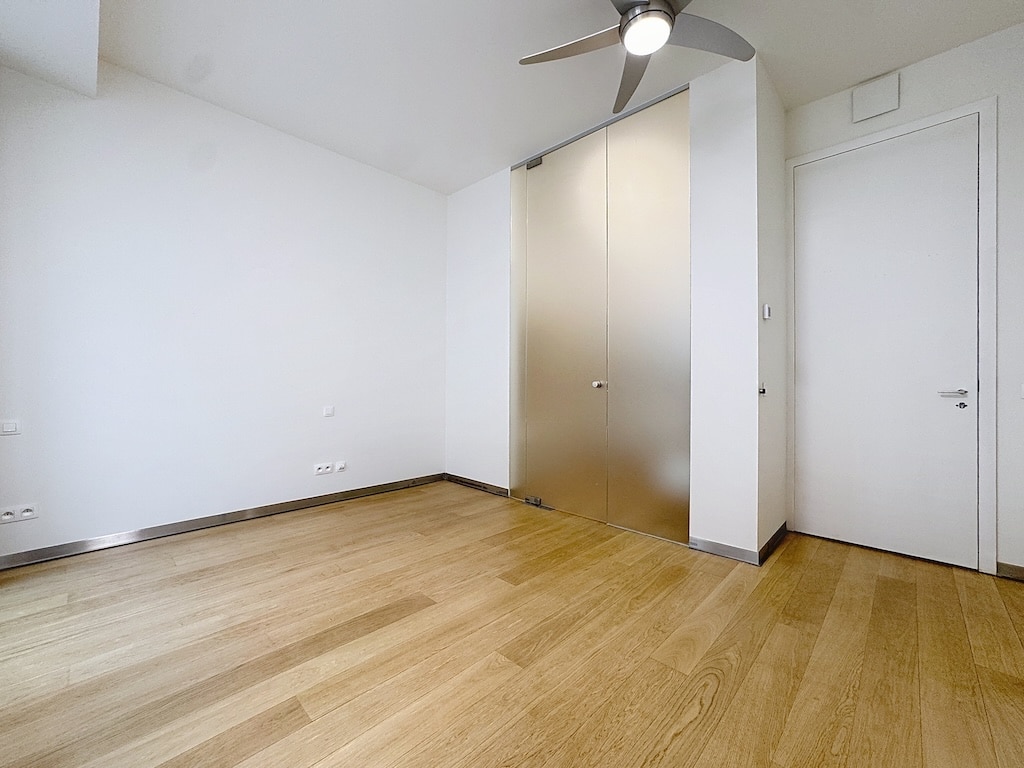 Salon minimaliste moderne avec sol en bois clair, armoire en verre dépoli et plafond avec ventilateur.