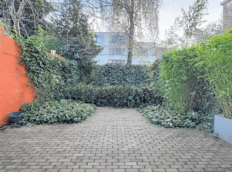 Jardin urbain paisible avec mur orange, bambous, chemin en briques et végétation abondante.
