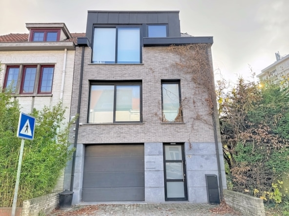 Maison moderne avec briques claires, grandes fenêtres panoramiques et contraste architectural élégant.