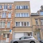 Rue urbaine avec bâtiments modernes, anciens, voitures et petits arbres.