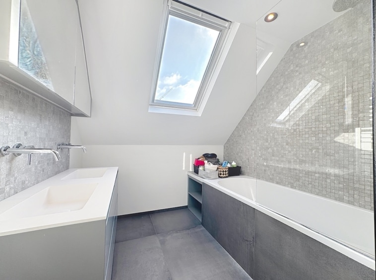 Salle de bain moderne lumineuse avec puits de lumière, design épuré et matériaux gris élégants.