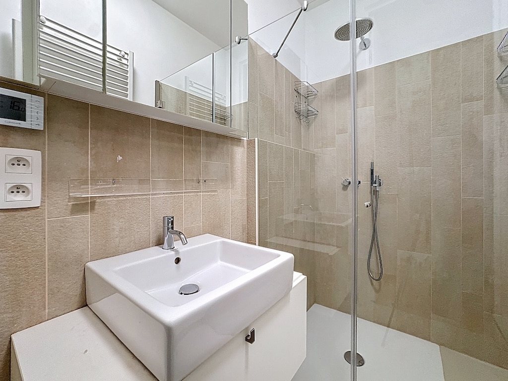 Salle de bain moderne compacte avec douche à litalienne, lavabo élégant et miroir mural.