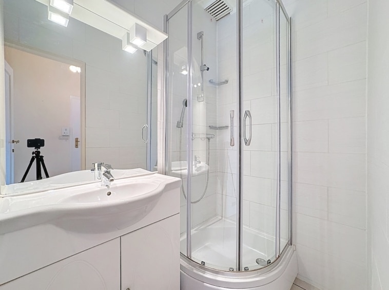 Salle de bain moderne avec douche en verre, vanity blanc et éclairage chaud.
