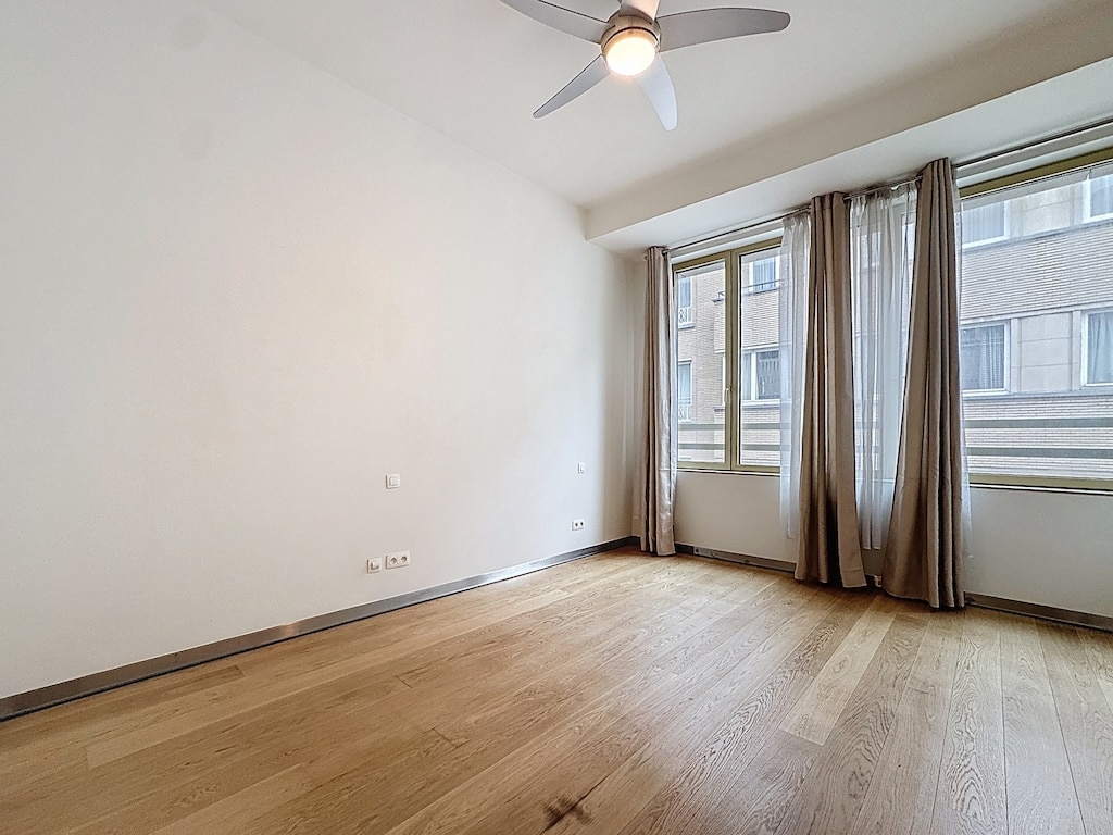 Salon lumineux minimaliste avec murs blancs, sol en érable et vue urbaine, ambiance chaleureuse.