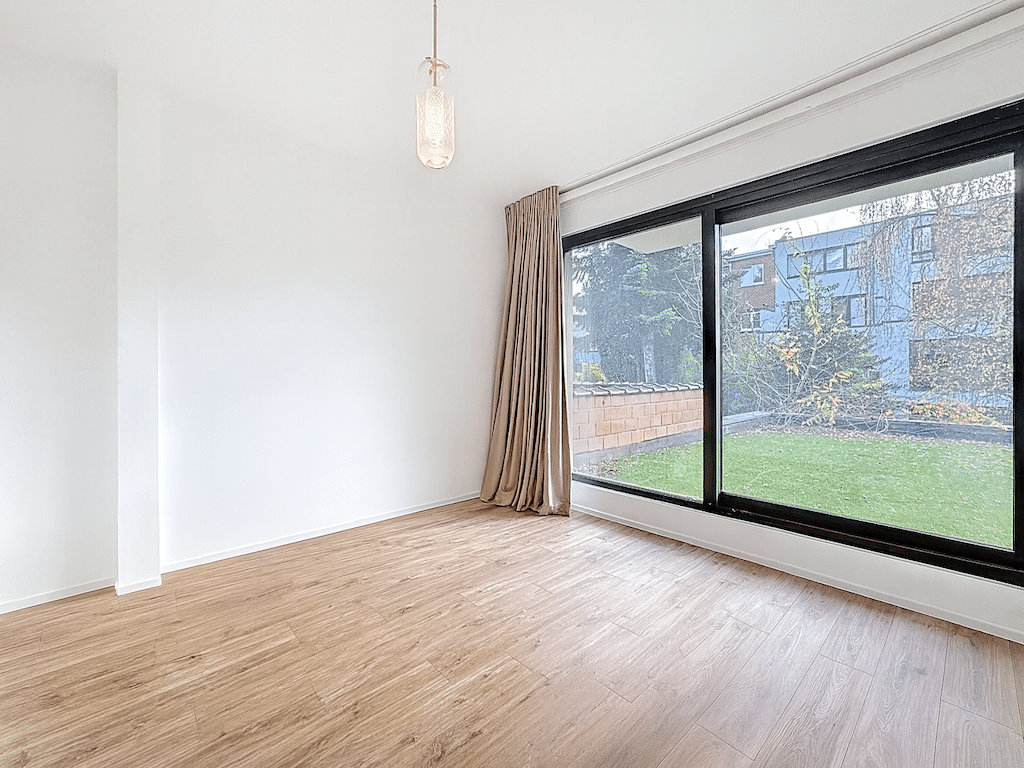 Salon moderne lumineux avec vue sur jardin verdoyant et éclairage suspendu élégant.