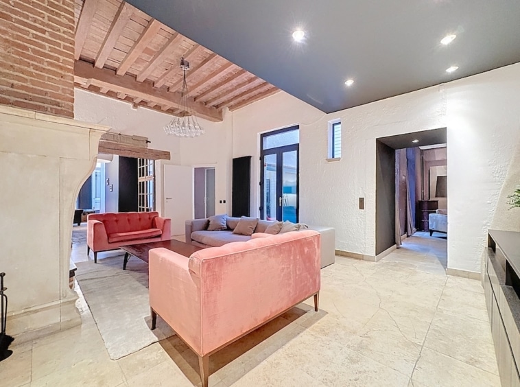 Salon moderne avec canapé rose velours, poutres en bois et luminosité naturelle.