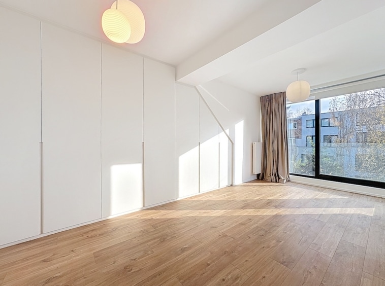 Salon lumineux moderne avec mobilier minimaliste, sol en bois clair et grande fenêtre naturelle.