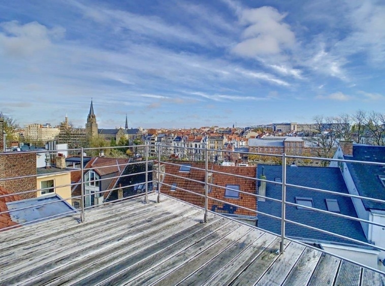 Vue dune terrasse urbaine offrant une vue sur les toits, clochers et ciel bleu lumineux.