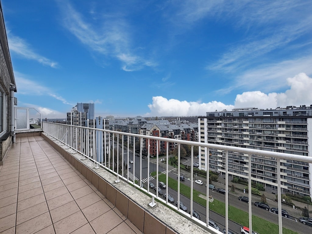 Balcon moderne avec vue sur ville, ciel bleu, bâtiments modernes et espace extérieur paisible.