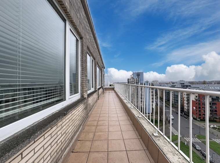 Balcon moderne surplombant une ville ensoleillée avec panorama urbain et ciel bleu.