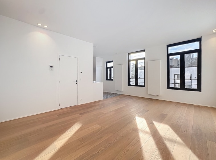 Intérieur moderne lumineux avec murs blancs, sol en bois clair, grandes fenêtres et design minimaliste.