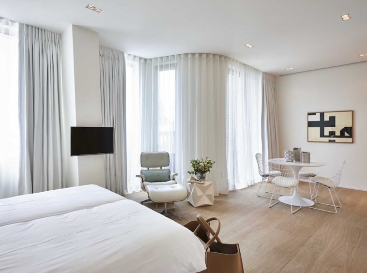 Chambre dhôtel moderne, lumineuse, épurée, avec lits confortables, coin lecture verte et espace repas élégant.