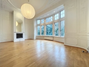 Salon contemporain lumineux avec murs blancs, grandes fenêtres, cheminée élégante, et éclairage moderne.