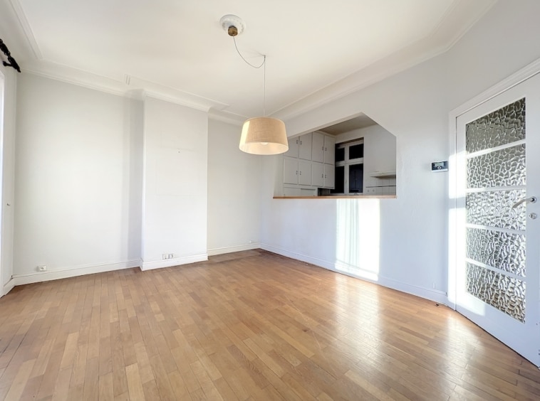 Intérieur lumineux avec cuisine ouverte moderne, sol en bois clair et grande fenêtre naturelle.