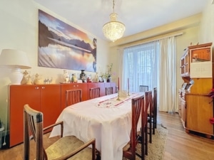 Salle à manger élégante avec grande table, chandelier classique, art apaisant, lumière naturelle abondante.