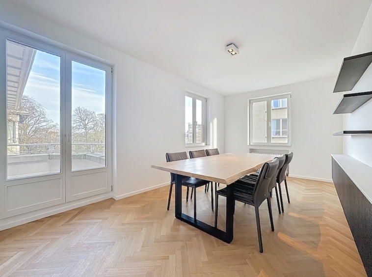 Salle à manger moderne lumineuse avec table en bois, chaises noires et grandes fenêtres.