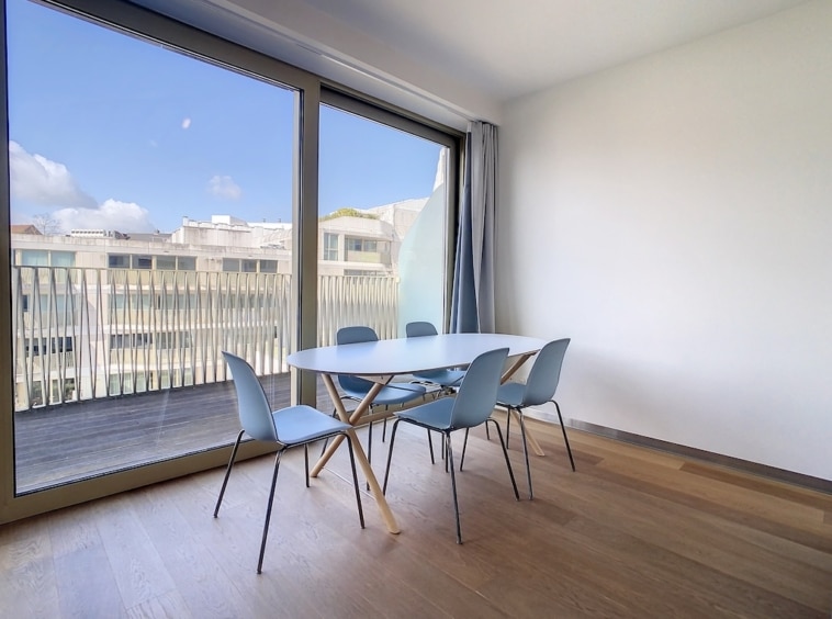 Salle à manger moderne en bois, lumineuse avec vue extérieure et mobilier bleu pastel.